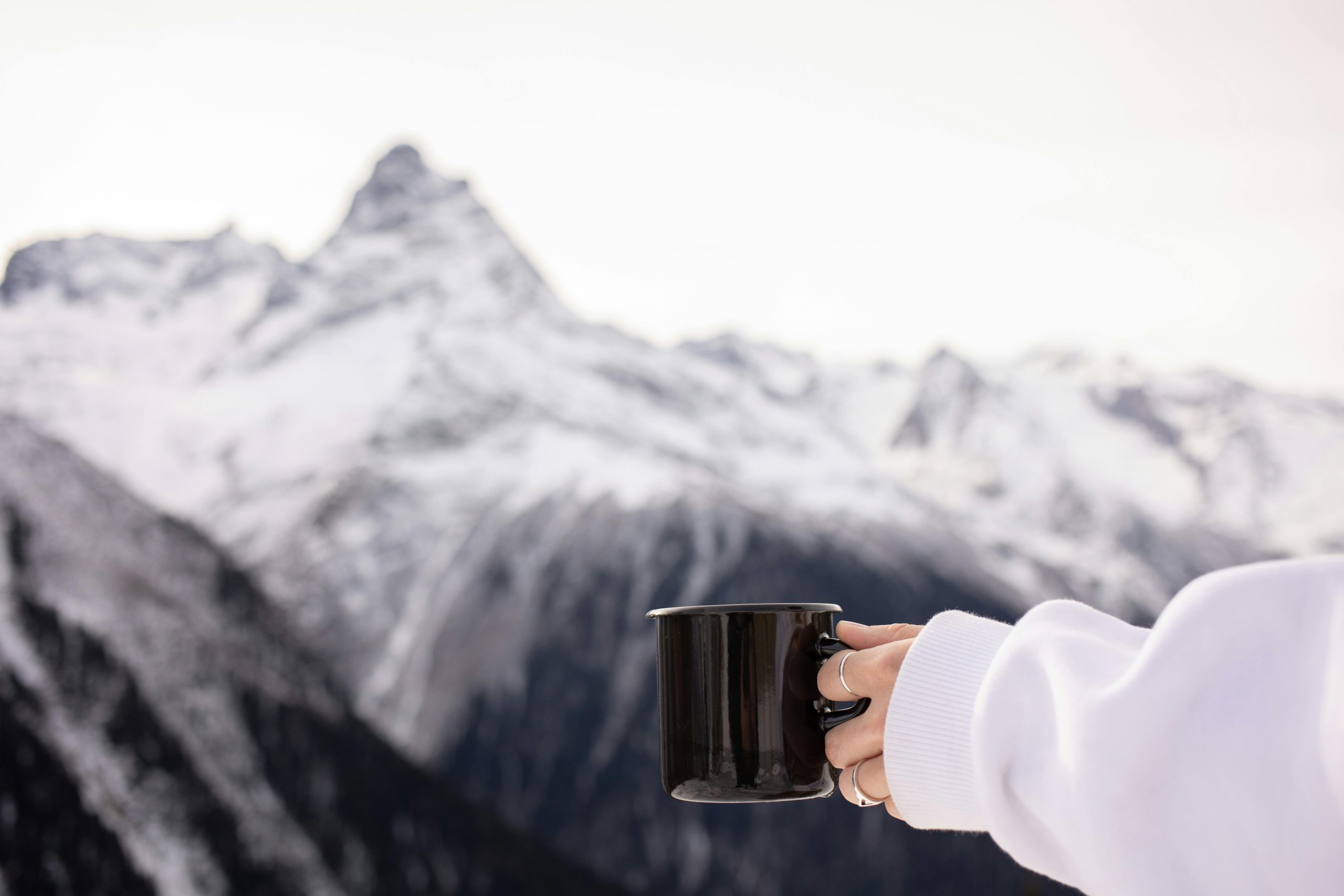 Woman holding a watch aloft at the peak of a snowy mountain.