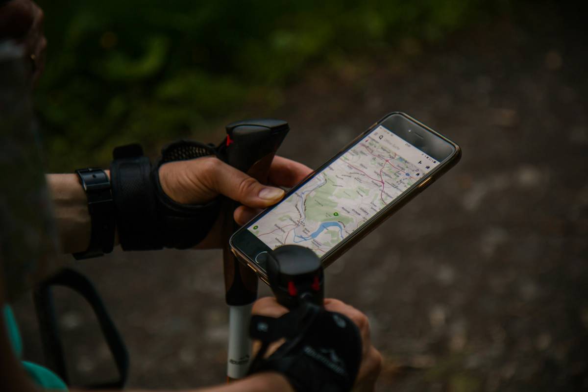 A hiker wearing a smartwatch checks the altimeter reading while standing near a rocky trail signpost.