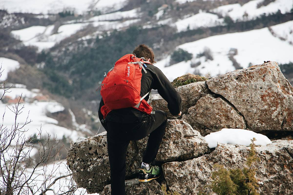 A woman wearing a sturdy jacket and an altimeter watch pointing toward mountains.